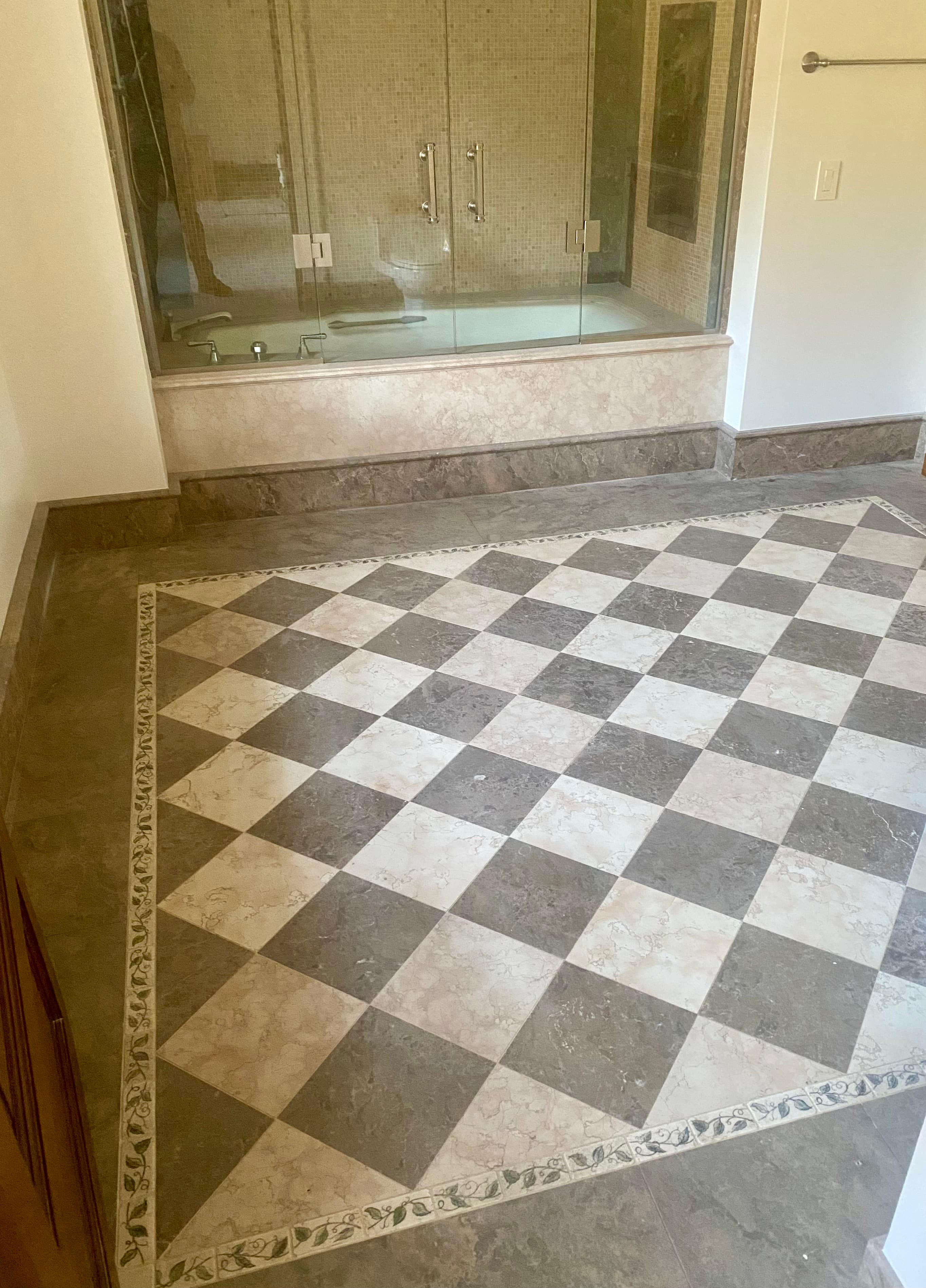 Grey and cream checkered tile floor with a decorative border and a glass-enclosed bathtub.