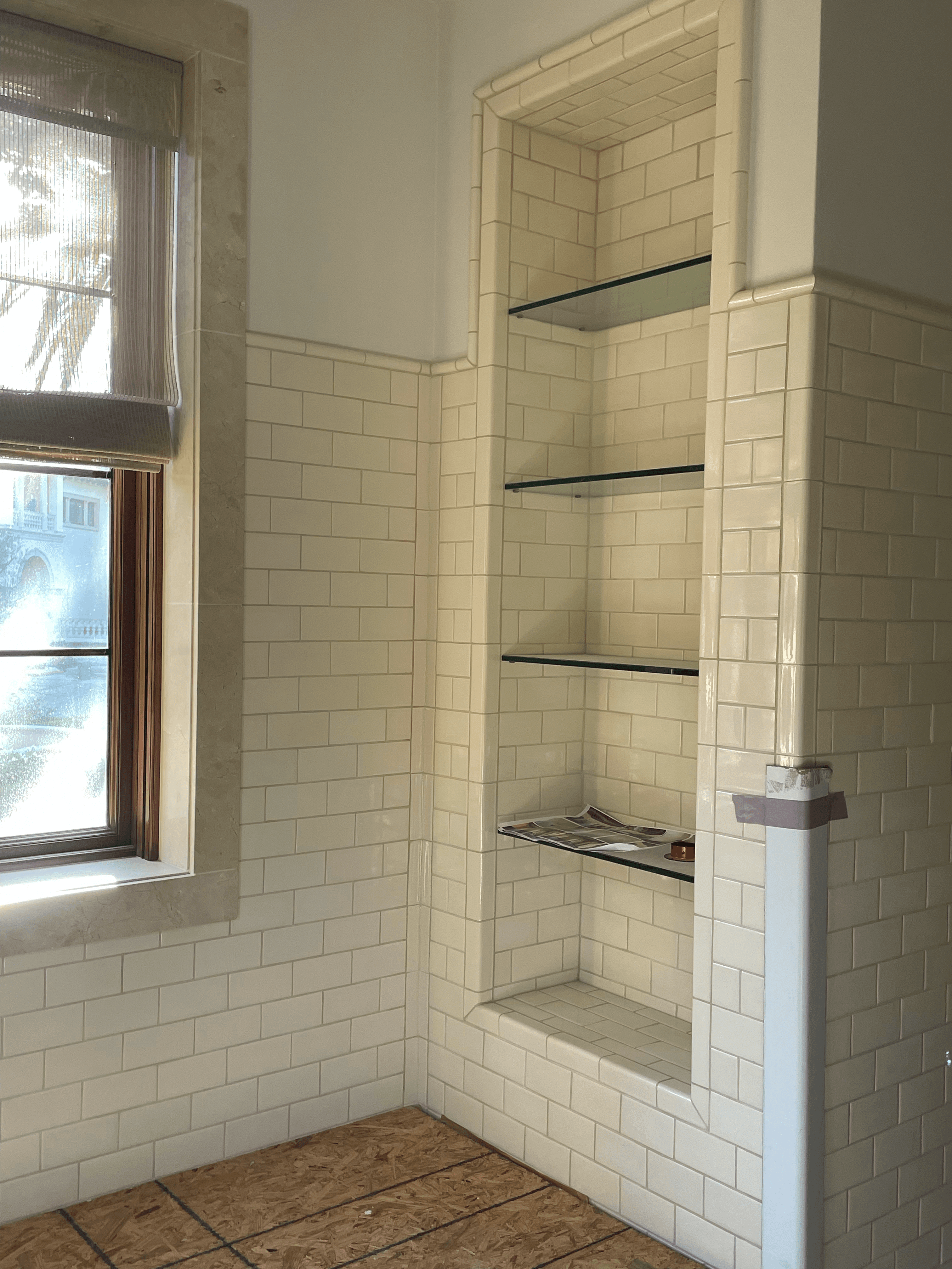 Cream subway tile walls with a built-in recessed alcove and glass shelves under renovation.